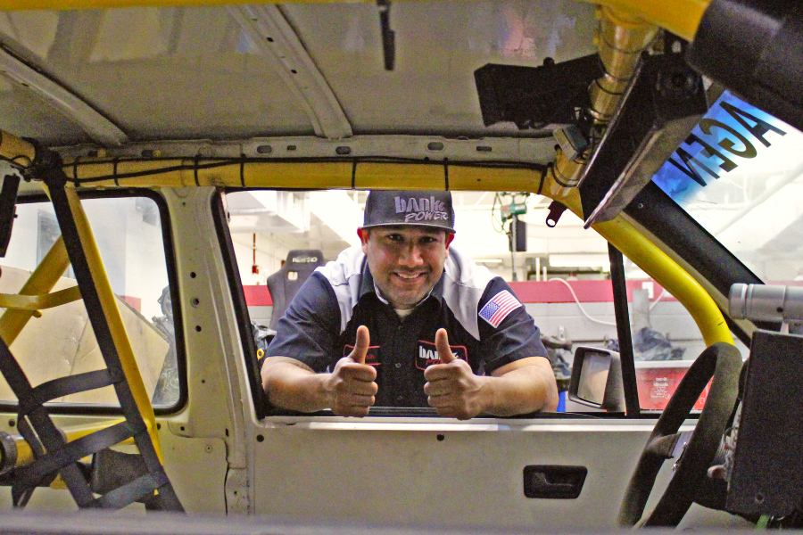 automotive technology alumnus gives a thumbs-up while working near a vehicle at an automotive performance shop