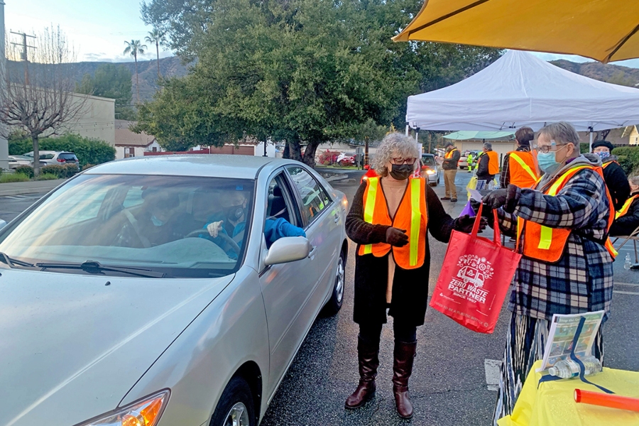 volunteers wearing safety vests and masks distribute items to a driver during the empty bowls drive thru fundraiser