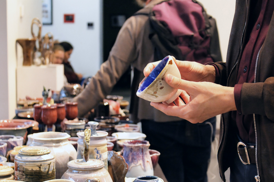 a shopper examines a handmade ceramic bowl among pottery displayed at the citrus college ceramics sale