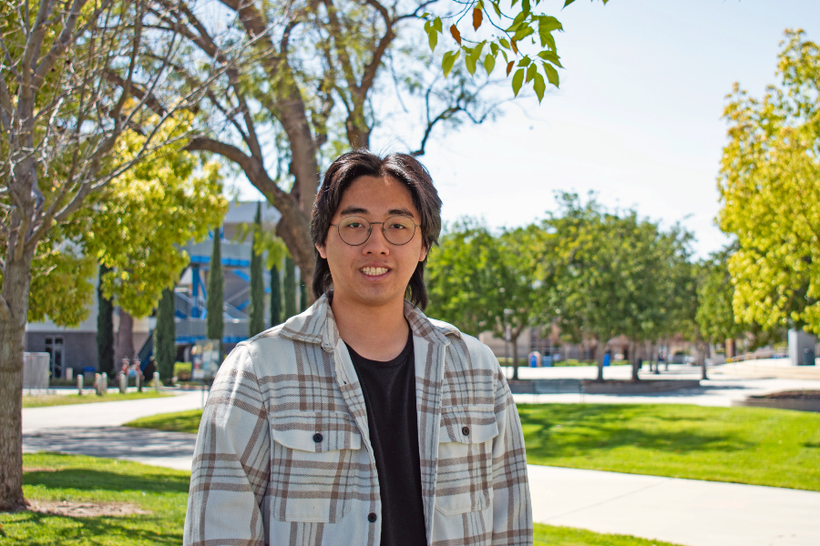 Quangnhan Duong standing outdoors on a college campus walkway near trees and lawn