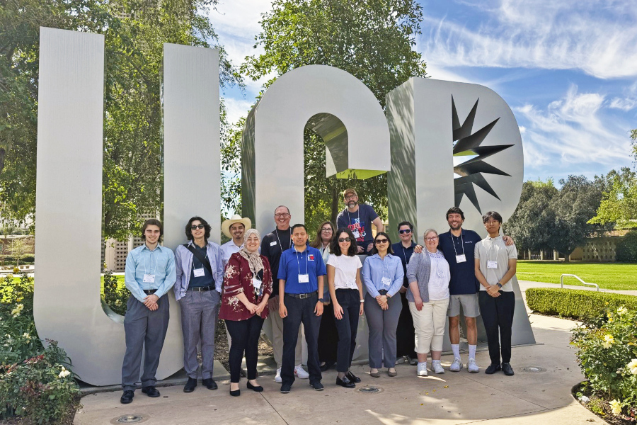 group of conference attendees pose in front of large ucr letters on a landscaped campus walkway