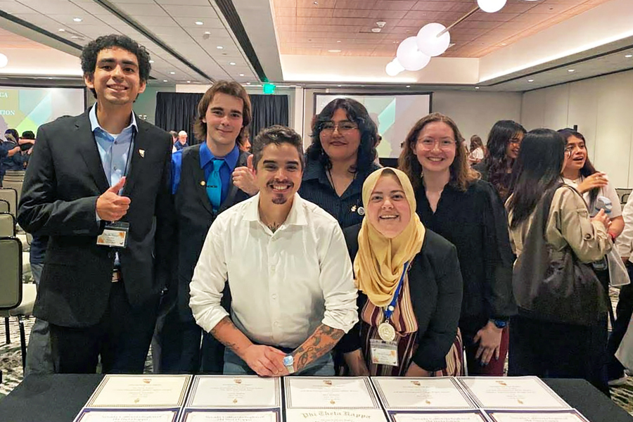 students pose together at an academic event with certificates displayed on a table in front of them