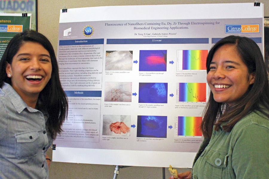 two citrus college students smile beside a research poster on fluorescent nanofibers during the stem research symposium