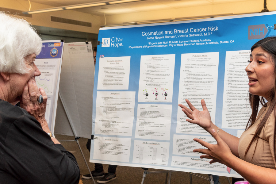 a student explains her cosmetics and breast cancer risk research poster to a visitor during the stem research symposium