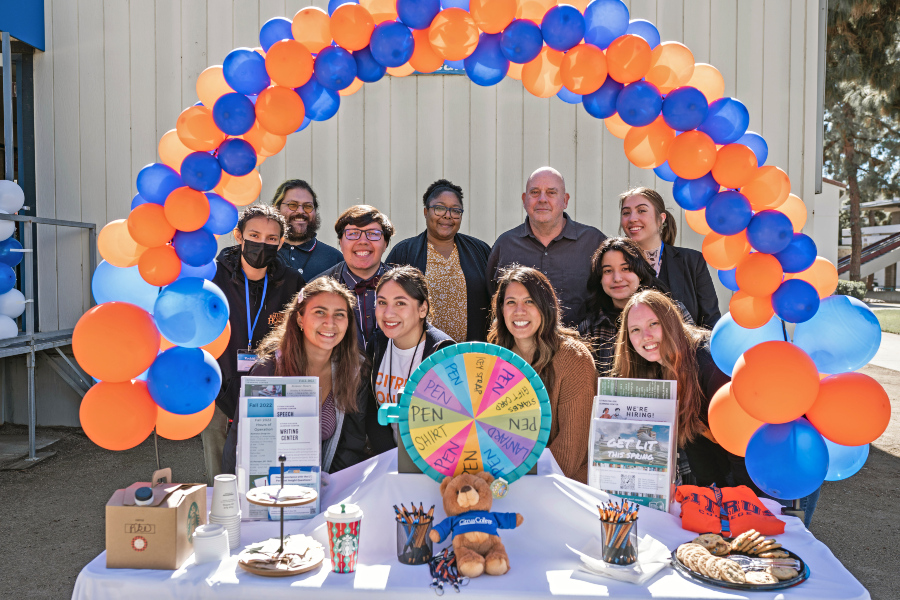 writing center staff and students gathered at an anniversary table under a blue and orange balloon arch