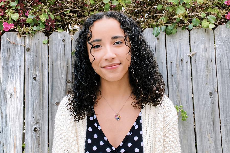 student smiles in front of a wooden fence covered with flowering vines