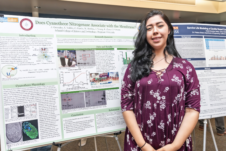student stands beside a research poster about cyanothece nitrogenase at a STEM research showcase
