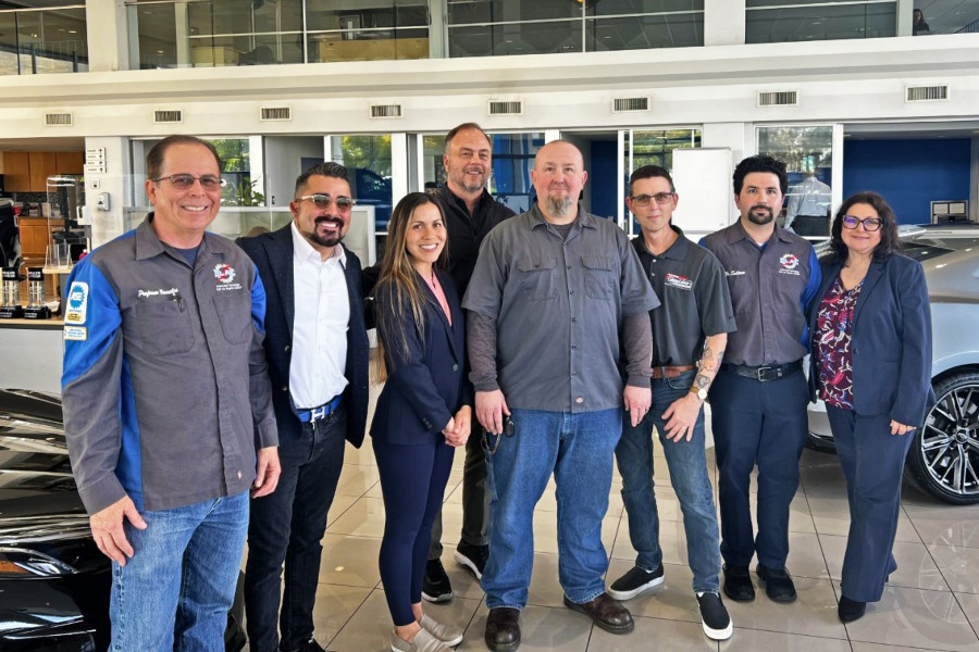 eight people standing in front of new cars in a car dealership showroom