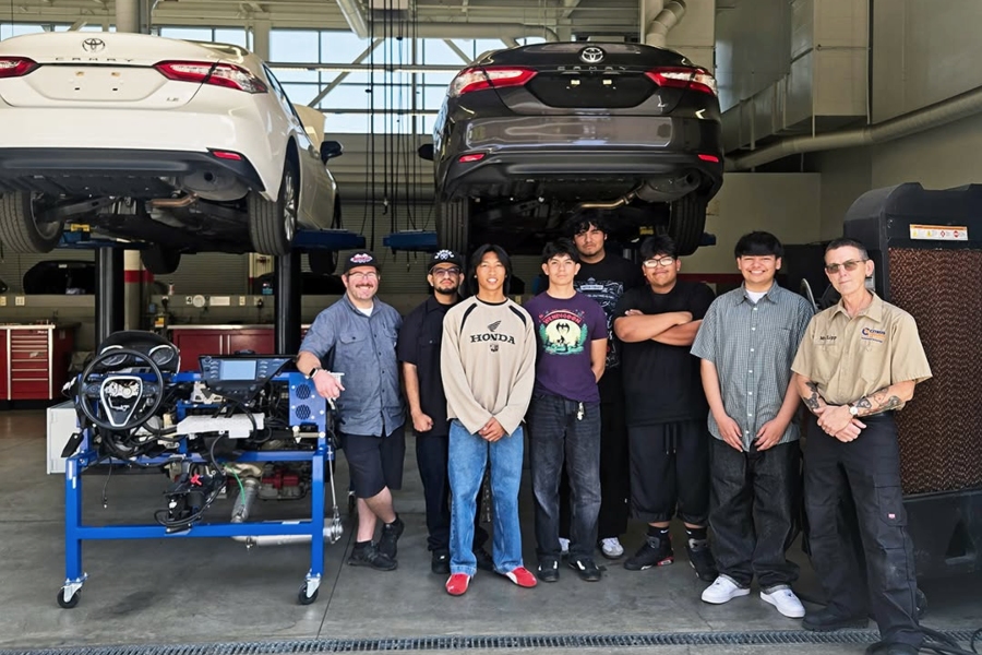 azusa high school students pose with citrus college automotive faculty member greg lipp inside an automotive laboratory, with two vehicles raised on lifts behind them