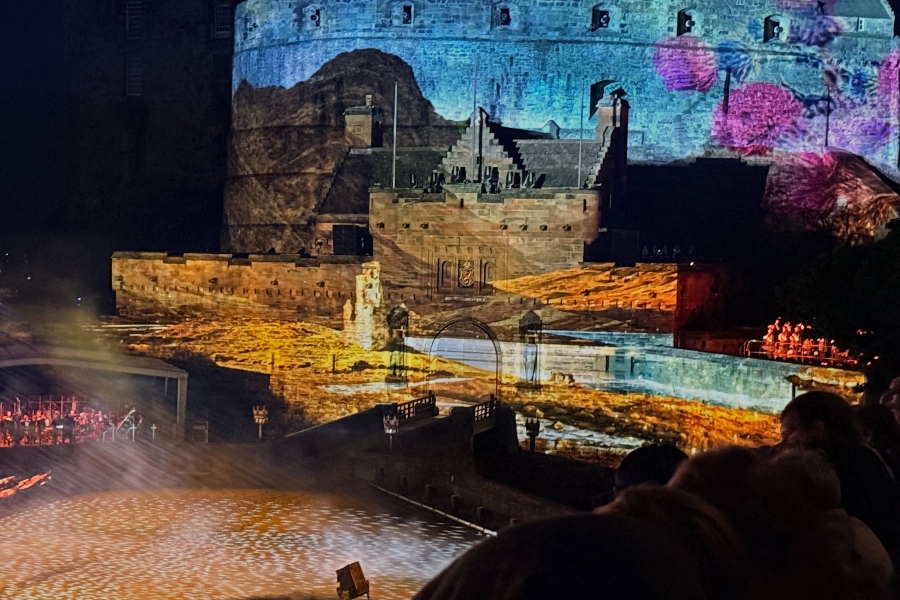 edinburgh castle illuminated with colorful projections during the royal edinburgh military tattoo, with performers and spectators visible around the esplanade
