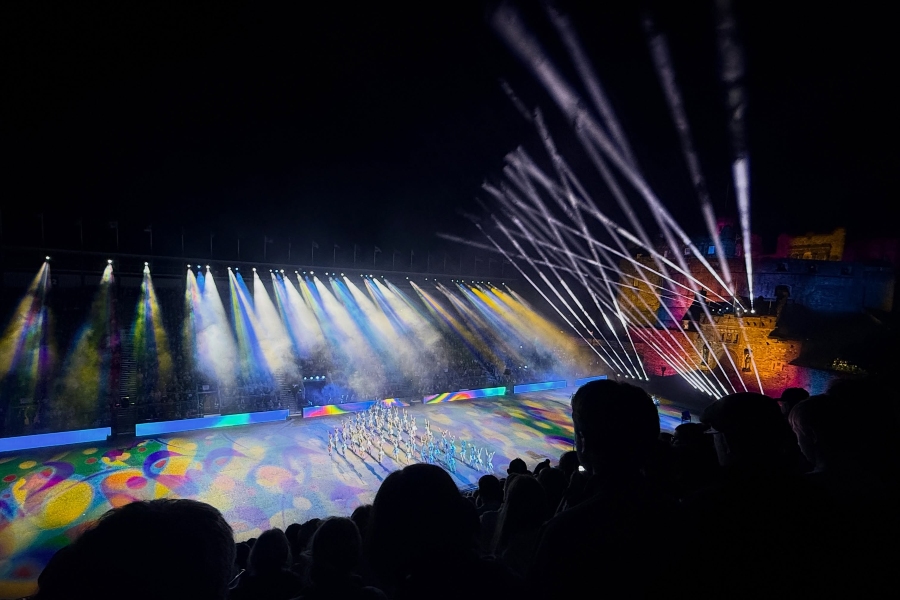 performers march across the esplanade at edinburgh castle as colorful projections and sweeping beams of light illuminate the royal edinburgh military tattoo