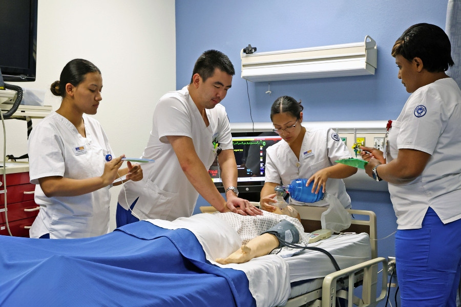 students in medical training uses a simulation mannequin to practice a clinical procedure while wearing gloves and a stethoscope in a lab setting