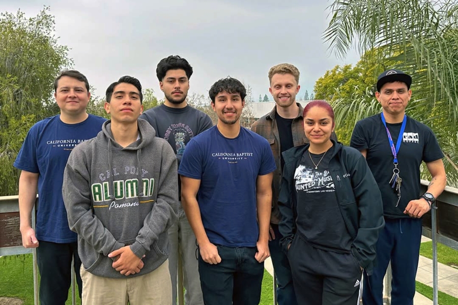 seven students stand together outdoors, several wearing university shirts representing california baptist university and cal poly pomona
