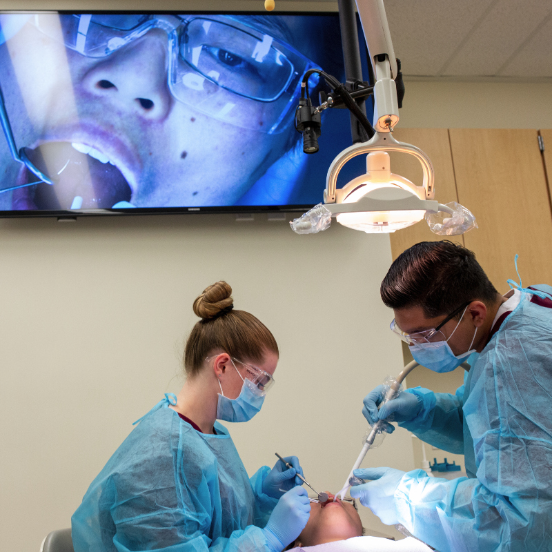 dental students in lab working on patient with video monitor overhead