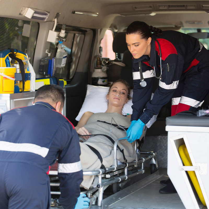 two EMTs loading a lady laying on a gurneyinto a transport vehicle