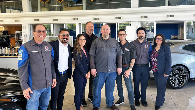 eight people standing in front of new cars in a car dealership showroom