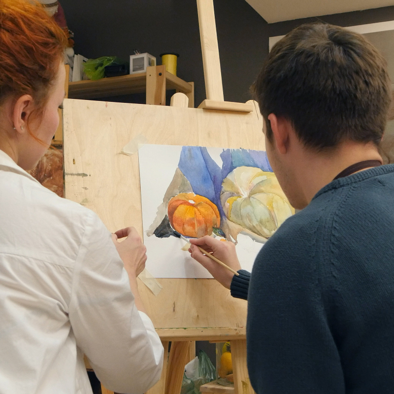 teacher assisting student with watercolor painting on a wooden easel