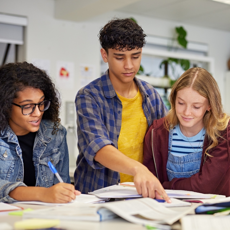 high school students working together at a table reviewing coursework and taking notes during a credit recovery or summer school class