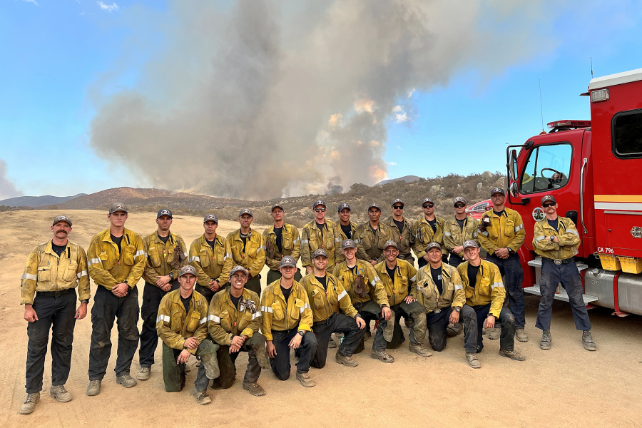 firefighters pose near a fire engine with smoke from the azusa canyon gulch fire rising in the background