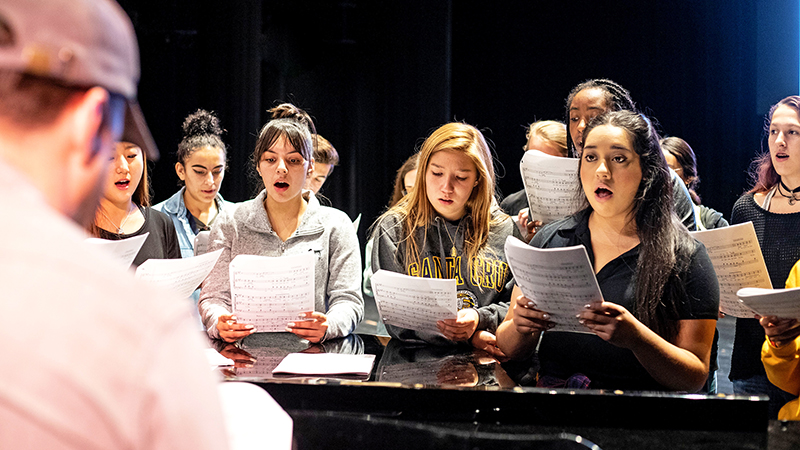 a group of diverse yourn students singing while holding sheet music