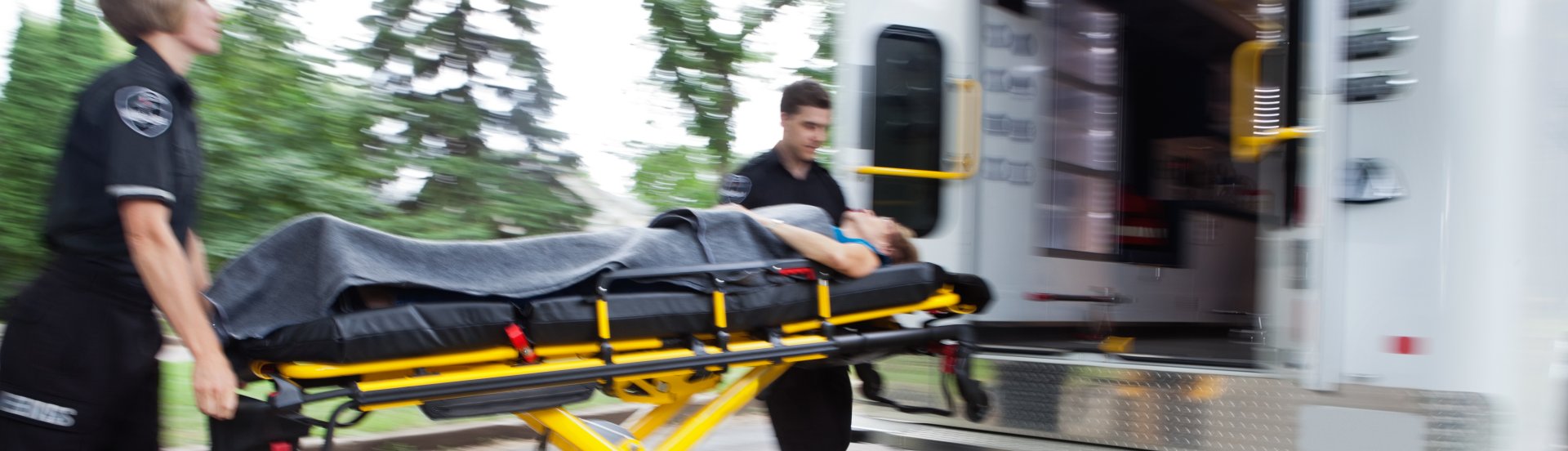 EMTs assisting a patient on a gurney in to an ambulance