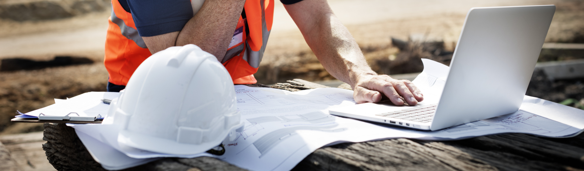 city employee with orange vest, laptop, construction hat and blueprints