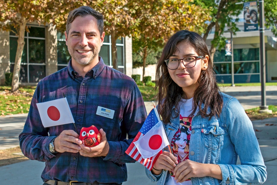 citrus college student and staff member hold japanese and u.s. flags and a daruma owl doll on campus