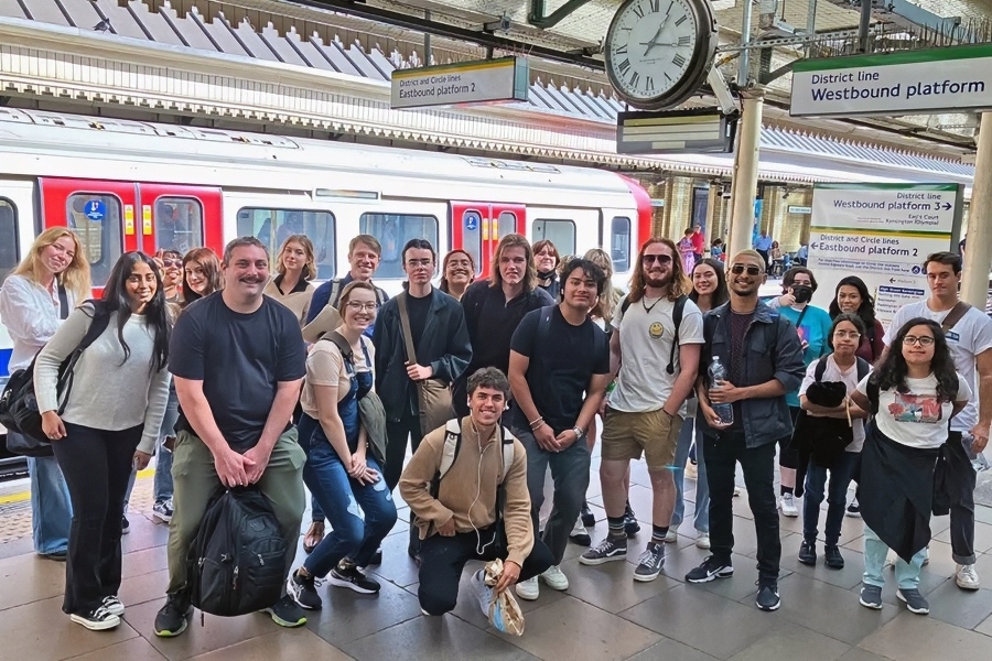 students gather on a london underground platform beside a train, with district and circle line signs and a large station clock visible overhead
