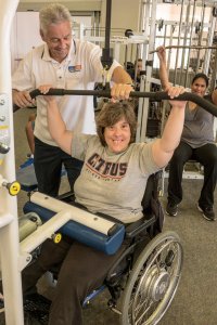 Female student using fitness equipment with the assistance of instructor