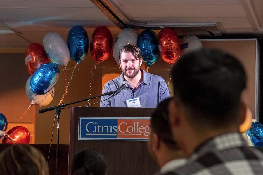 a student speaker addresses guests from a citrus college podium during the foundation's scholarship reception, with orange, white and blue balloons behind him
