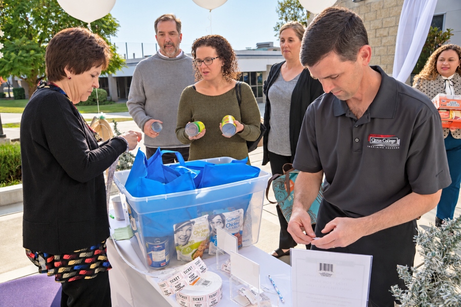 citrus college faculty and staff sort canned food donations reusable bags and raffle tickets at an outdoor holiday giving event supporting the campus food pantry