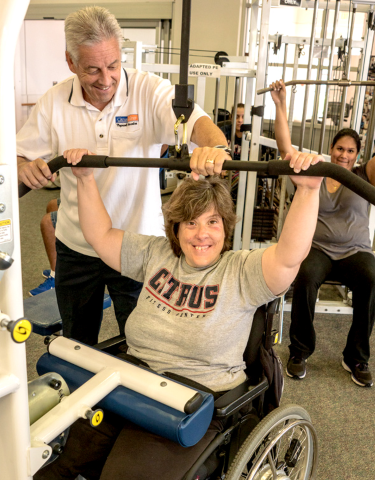 fitness instructor provides assistance to a student with a wheelchair-accessible weight machine