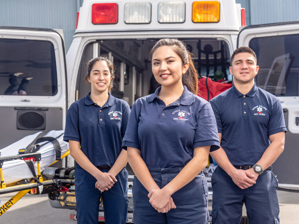 three Citrus College EMT students with a gurney and an emergency response vehicle in the background