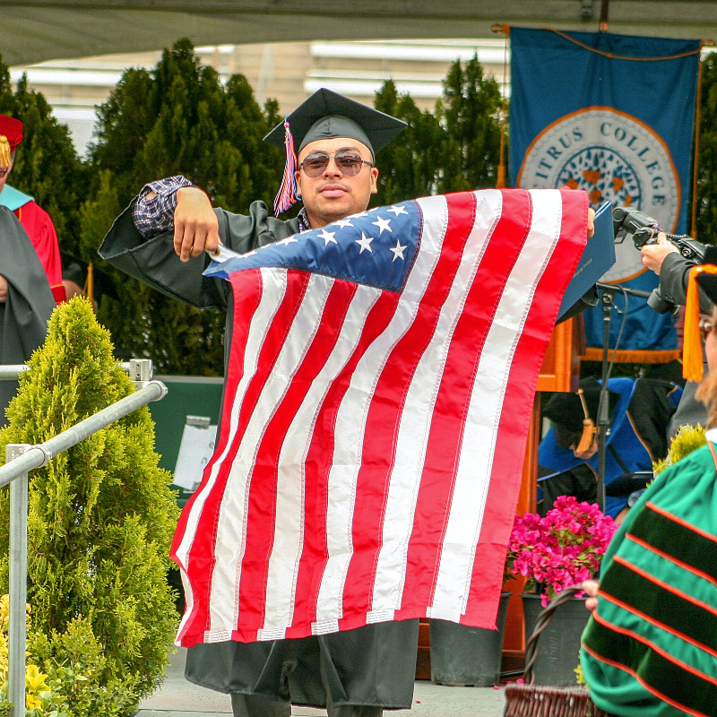 student-veteran graduate walking down the rampafter receiving diploma proudly carrying the U.S. flag