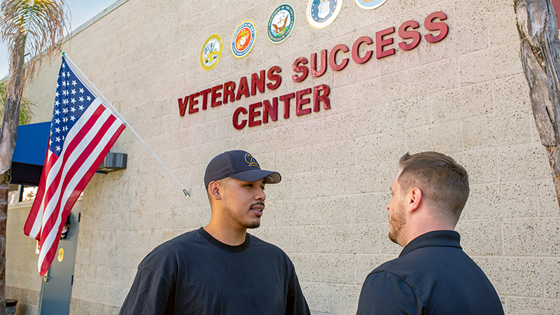 Two student veterans standing outside the Veterans Success Center with an American flag in the background