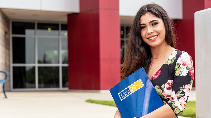 Latina student standing at the entrance of the college's Student Services Building