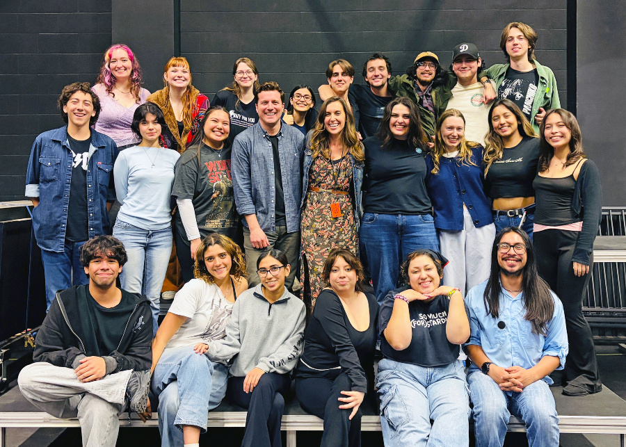 group of college theater students and staff posing together on stage, smiling in casual attire during rehearsal for a new stage production