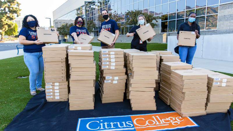 college staff in masks with stacks of boxed Chromebooks