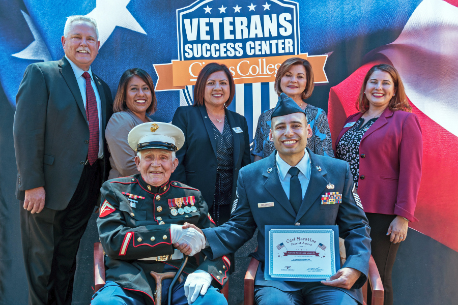 a world war II marine veteran shakes hands with an air force reservist holding the carl harstine patriot award as citrus college representatives stand behind them