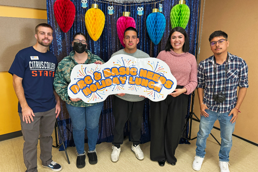 students and staff holding a dream resources center and basic needs holiday lunch sign in front of colorful decorations
