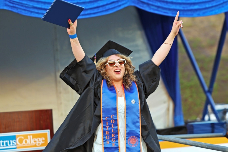 graduate in cap and gown celebrates on stage while holding a diploma cover during citrus college commencement