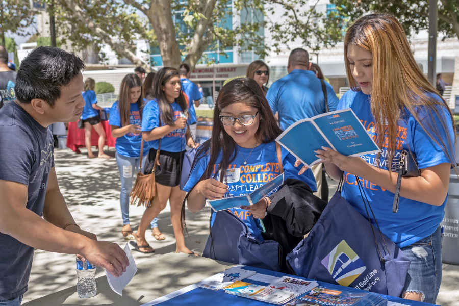 students receive information at a citrus college early decision welcome day table while holding campus materials