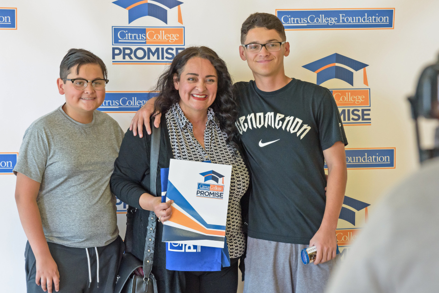 a woman and two students pose in front of a citrus college promise and foundation backdrop during parent night