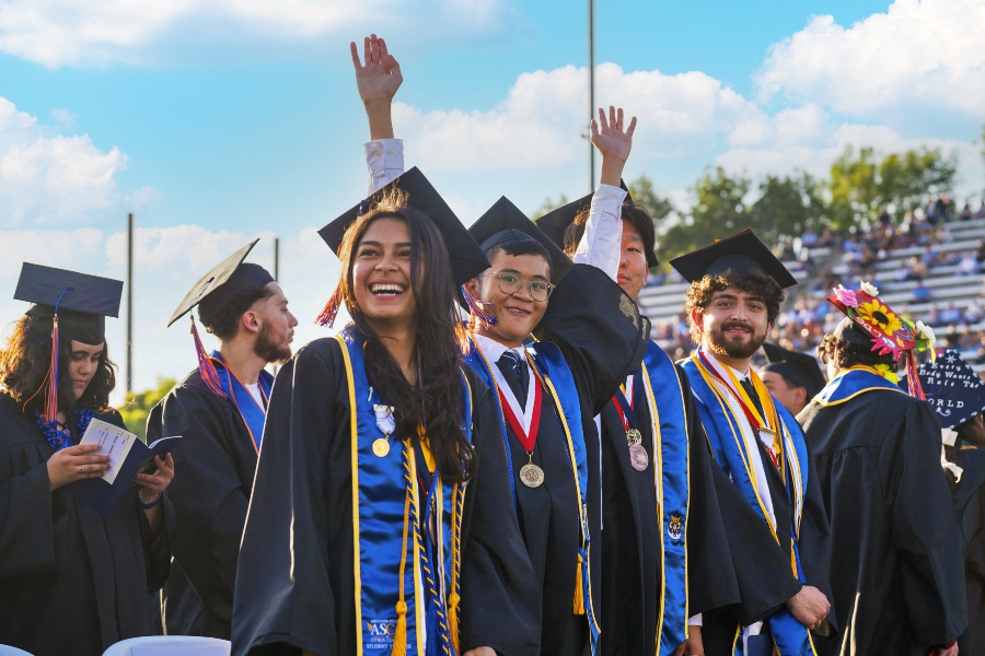 students in caps and gowns celebrate during citrus college commencement while standing in front of stadium bleachers