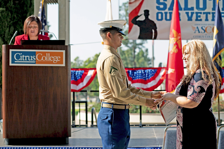 a uniformed service member shakes hands with a woman holding a certificate during a veterans ceremony at citrus college