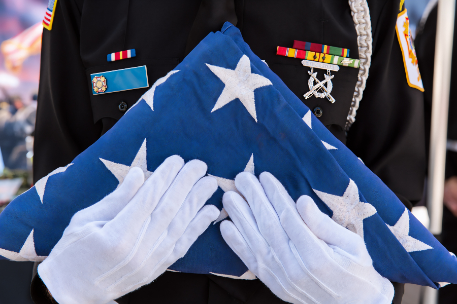 a uniformed honor guard wearing white gloves holds a folded american flag during a veterans ceremony