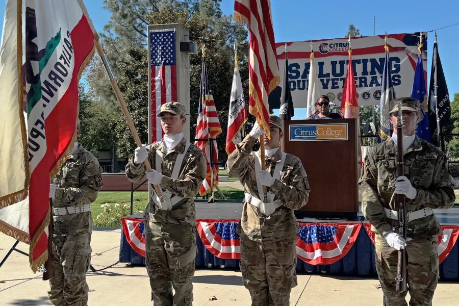 citrus college rotc cadets present the colors during a saluting our veterans ceremony as a speaker stands at the podium behind them, with american, california and military flags displayed around the stage