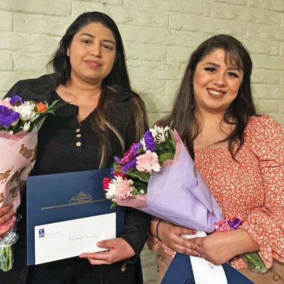 two scholarship recipients holding flowers and certificates at an award ceremony