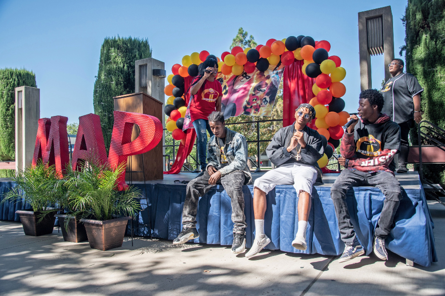 guardian scholars perform on an outdoor stage decorated with red, orange and black balloons and large illuminated MAP letters