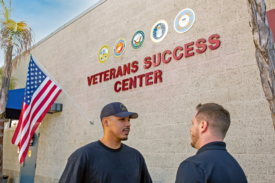 Two student veterans standing outside the Veterans Success Center with an American flag in the background